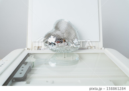 A silver disco-ball heart rests on a flatbed scanner, its mirrored tiles catching and scattering light to create playful reflections and a surreal blend of romance, glamour, and scanning technology. A silver disco-ball heart rests on a flatbed scanner, its mirrored tiles catching and scattering light to create playful reflections and a surreal blend of romance, glamour, and scanning technology. 138861284