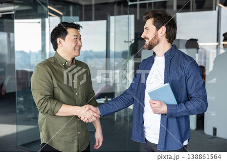 Two smiling multiethnic businessmen shaking hands, making a professional greeting and showing their partnership and collaboration in a modern office meeting Two smiling multiethnic businessmen shaking hands, making a professional greeting and showing their partnership and collaboration in a modern office meeting 138861564