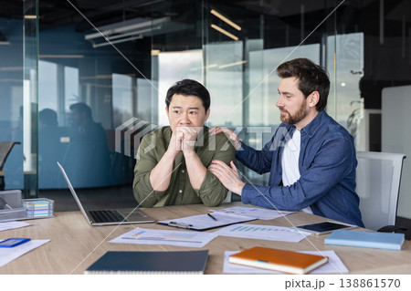Male colleague offers empathetic support to stressed asian businessman at his office desk, consoling him during a moment of anxiety, burnout and workplace distress Male colleague offers empathetic support to stressed asian businessman at his office desk, consoling him during a moment of anxiety, burnout and workplace distress 138861570