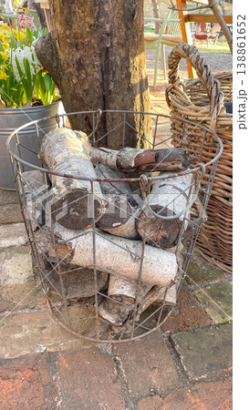 Birch firewood logs Betula pendula in a metal wire basket on a rustic stone pavement in spring garden 138861652
