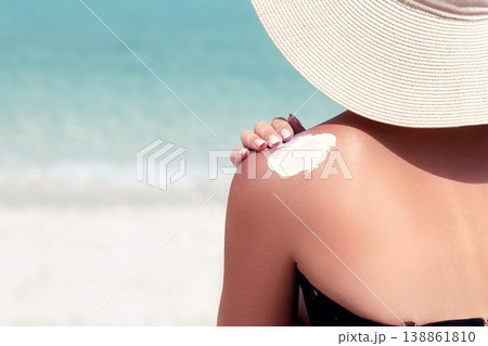 Woman applying sunscreen creme on tanned shoulder. Skincare. Sun protection sun cream. Bikini hat woman applying sunscreen lotion on back Woman applying sunscreen creme on tanned shoulder. Skincare. Sun protection sun cream. Bikini hat woman applying sunscreen lotion on back 138861810