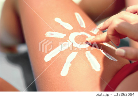 Sunbath protection. Woman using Suntan Lotion At The Beach In Form Of The Sun on leg 138862084