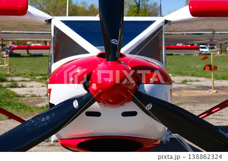 Red and white light sport aircraft propeller hub closeup with three blades against airfield background Red and white light sport aircraft propeller hub closeup with three blades against airfield background 138862324