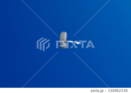 Skydiver parachutist descending with white parachute and white flag against clear blue sky Skydiver parachutist descending with white parachute and white flag against clear blue sky 138862336