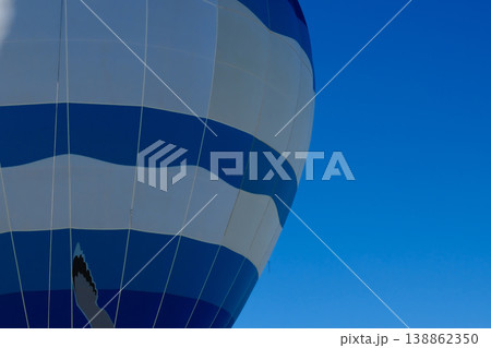Low angle upward view of blue and white striped hot air balloon envelope against clear blue sky Low angle upward view of blue and white striped hot air balloon envelope against clear blue sky 138862350