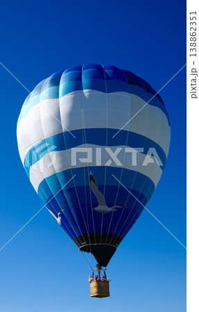 Blue and white striped hot air balloon with basket floating against deep clear blue sky sunny day Blue and white striped hot air balloon with basket floating against deep clear blue sky sunny day 138862351