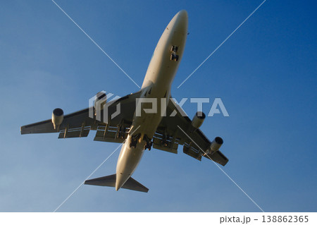 Commercial passenger airplane flying overhead viewed from below against pale blue sky on sunny daytime Commercial passenger airplane flying overhead viewed from below against pale blue sky on sunny daytime 138862365