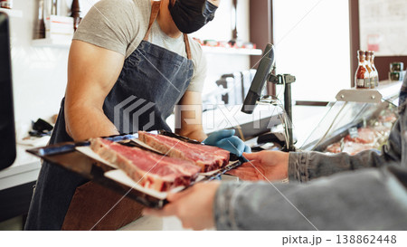Butcher sells fresh meat to customer in shop with clear hygiene measures Butcher sells fresh meat to customer in shop with clear hygiene measures 138862448