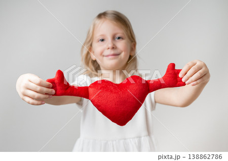 Front view. A cute little girl is holding a soft toy in the shape of a heart 138862786