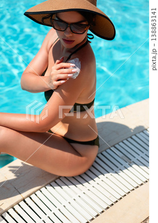 Pretty Woman Applying Sunscreen On Shoulder Sitting By Poolside Close View In Summer Sunlight. Skincare And Sun Protection Concept With Healthy Skin Glow Pretty Woman Applying Sunscreen On Shoulder Sitting By Poolside Close View In Summer Sunlight. Skincare And Sun Protection Concept With Healthy Skin Glow 138863141