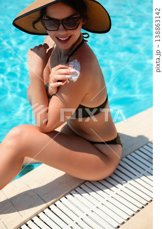 Beautiful Woman Smiling While Applying Sunscreen On Shoulder Sitting By Pool. Summer Skincare Routine And Sun Protection Concept With Healthy Skin Glow Beautiful Woman Smiling While Applying Sunscreen On Shoulder Sitting By Pool. Summer Skincare Routine And Sun Protection Concept With Healthy Skin Glow 138863142
