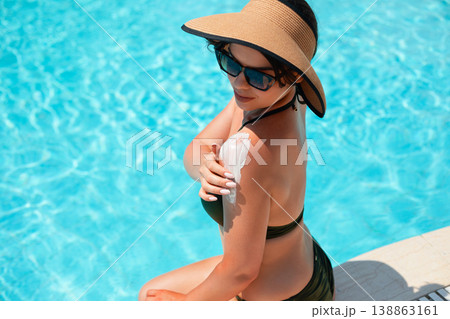 Beautiful Woman Applying Sunscreen On Shoulder Sitting By Poolside In Bright Light. Summer Skincare Routine And Sun Protection Concept Beautiful Woman Applying Sunscreen On Shoulder Sitting By Poolside In Bright Light. Summer Skincare Routine And Sun Protection Concept 138863161