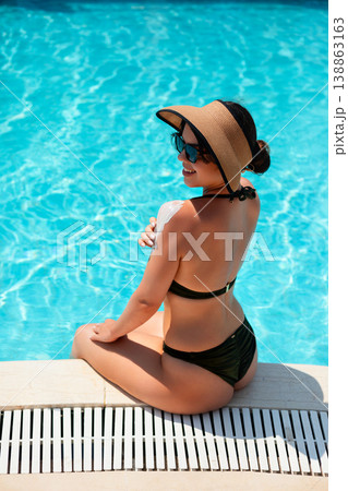 Beautiful Woman Sitting By Poolside Relaxing After Applying Sunscreen In Bright Summer Sunlight. Skincare And Healthy Lifestyle Concept 138863163
