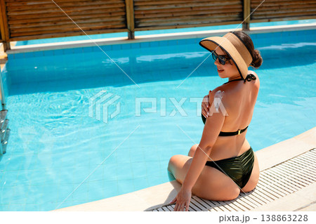 Attractive Woman Sitting by Pool with Sunscreen on Back in Summer Sun. Skincare Routine Concept 138863228