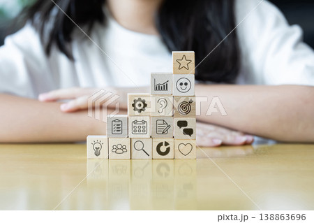 Wooden blocks with simple icons form rising steps on a table. A child in soft blur suggests learning progress and steady development. 138863696