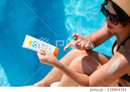 Top View Of Woman Holding Sunscreen Bottle And Applying Cream On Shoulder Sitting By Poolside In Bright Sunlight 138864191