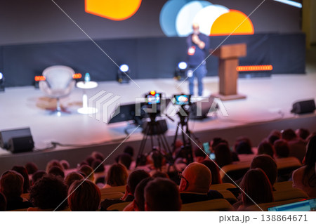 Conference speaker on stage with cameras and attentive audience during live presentation Conference speaker on stage with cameras and attentive audience during live presentation 138864671
