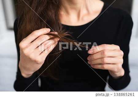 womans hands examine the ends of her long brown hair in close-up. personal care beauty routine health hair damage check concept womans hands examine the ends of her long brown hair in close-up. personal care beauty routine health hair damage check concept 138865261