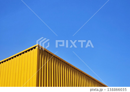 Modern industrial building with vibrant yellow corrugated metal walls set against a clear blue sky. Modern industrial building with vibrant yellow corrugated metal walls set against a clear blue sky. 138866035