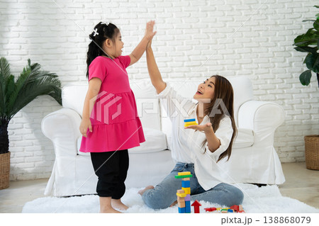 A mother shares a joyful moment with her autistic daughter in a cozy living room. Surrounded by colorful toys, the scene highlights neurodiversity, emotional bonding, and inclusive family life 138868079
