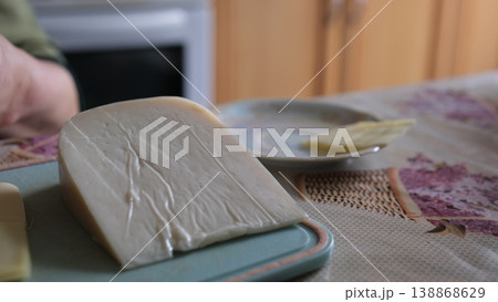 Elderly woman preparing cheese removing packaging slicing on wooden board homemade kitchen closeup Elderly woman preparing cheese removing packaging slicing on wooden board homemade kitchen closeup 138868629