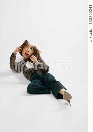 Young woman lying on floor holding printed face panel creative fashion studio portrait Young woman lying on floor holding printed face panel creative fashion studio portrait 138869241