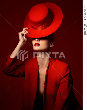 Hat, fashion and a model woman on a red background in studio for elegant or trendy style. Aesthetic, art and beauty with a confident young female person posing in an edgy, classy or unique suit Hat, fashion and a model woman on a red background in studio for elegant or trendy style. Aesthetic, art and beauty with a confident young female person posing in an edgy, classy or unique suit 138870960