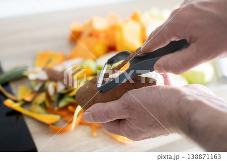 Peeling potato with peeler during vegetable preparation in kitchen 138871163