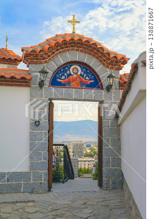 Plovdiv church gate with stone arch and religious icon overlooking cityscape through entrance of Saints Archangels church in Plovdiv Bulgaria. Concept of religion heritage, travel culture 138871667