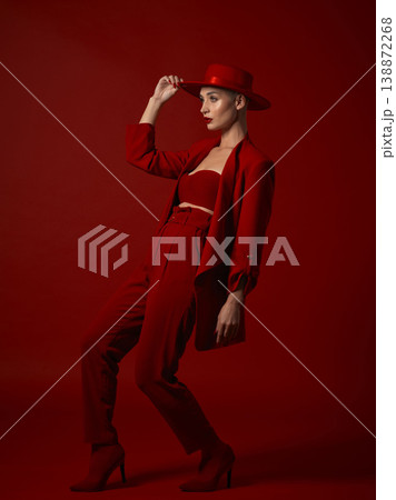 Aesthetic, fashion and a woman walking on a red studio background for elegant or trendy style. Runway model, art or beauty with a confident young female person looking edgy and classy in a bold suit 138872268
