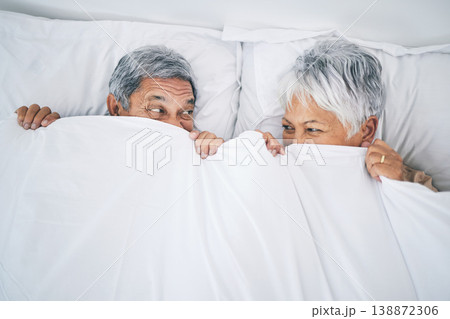 Bed, funny and senior couple covering with a blanket in a bedroom bonding as happiness and playing to enjoy retirement. Happy, goofy and elderly people, man and woman with trust in marriage in a home 138872306