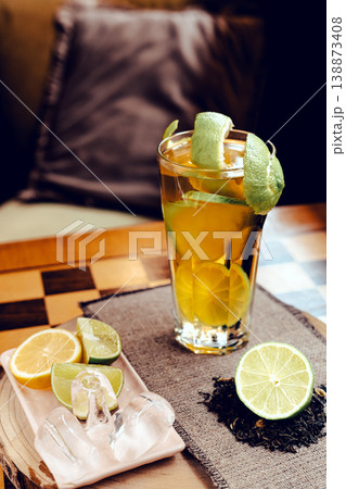 A glass of iced tea with a splash of lime juice, garnished with lime zest, placed on a coffee table, refreshing summer drink, natural light, minimal composition. A glass of iced tea with a splash of lime juice, garnished with lime zest, placed on a coffee table, refreshing summer drink, natural light, minimal composition. 138873408