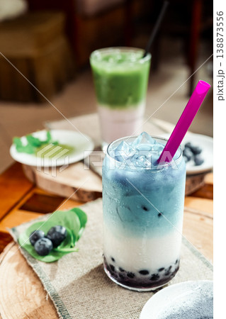A refreshing blueberry milk drink with a vibrant blue color and whole berries, garnished with mint leaves, blueberries, and matcha powder, natural light, minimal composition. A refreshing blueberry milk drink with a vibrant blue color and whole berries, garnished with mint leaves, blueberries, and matcha powder, natural light, minimal composition. 138873556