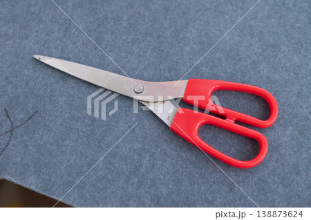 Red-handled scissors on gray felt fabric surface Red-handled scissors on gray felt fabric surface 138873624