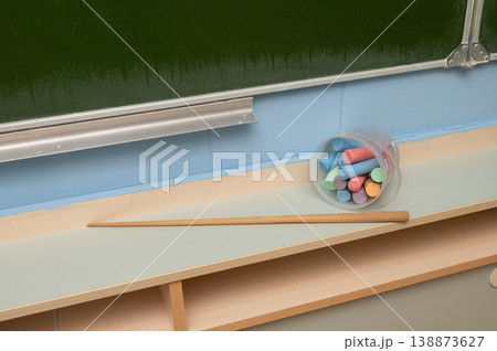 Chalk sticks and wooden pointer on classroom desk against blackboard 138873627
