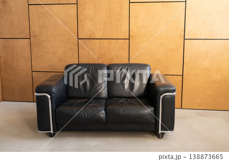 Black leather two seat sofa placed against wooden panels 138873665