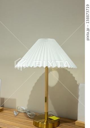 Elegant brass table lamp with white pleated shade on wooden surface Elegant brass table lamp with white pleated shade on wooden surface 138873719
