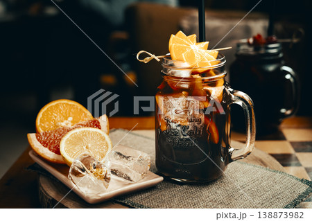 Citrus iced tea with added strawberry juice, decorated with fresh orange served in a glass mug, standing on a coffee table. Natural light, minimalism. 138873982