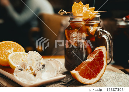 Citrus iced tea with added strawberry juice, decorated with fresh orange served in a glass mug, standing on a coffee table. Natural light, minimalism. Citrus iced tea with added strawberry juice, decorated with fresh orange served in a glass mug, standing on a coffee table. Natural light, minimalism. 138873984