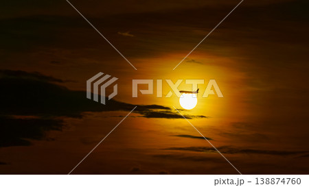 Tokyo, Japan - Oct 2 2024, Panoramic view of the bright orange sunset sun among dark clouds, silhouette of an airplane flies past the sun, Tokyo, Japan 138874760