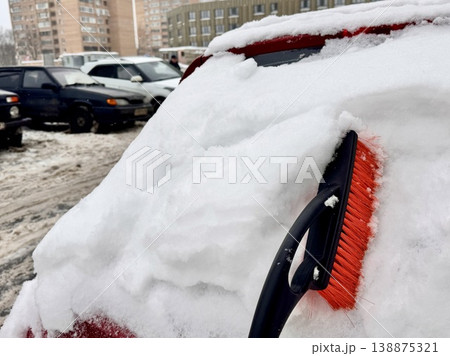 car brush with a scraper in black and orange on a background of snow-white snow on a car in winter 138875321