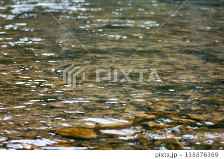 Clear water flowing over smooth stones in a river bed. Natural texture of creek bottom with ripples and reflections. Environmental concept of clean stream, wildlife and wilderness. Clear water flowing over smooth stones in a river bed. Natural texture of creek bottom with ripples and reflections. Environmental concept of clean stream, wildlife and wilderness. 138876369