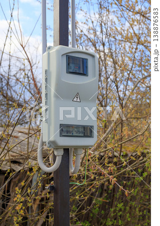 Outdoor electric meter box mounted on a metal pole in a rural area. Plastic electrical cabinet with circuit breakers and high voltage sign. 138876583