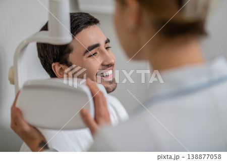 Dentist adjusting x-ray equipment near patient face Dentist adjusting x-ray equipment near patient face 138877058