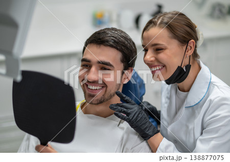 Happy patient and dentist looking at smile in mirror Happy patient and dentist looking at smile in mirror 138877075