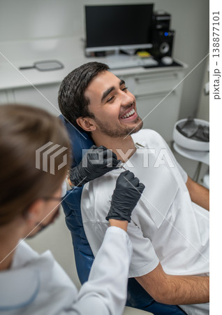 Female dentist fixing bib on smiling patient 138877101