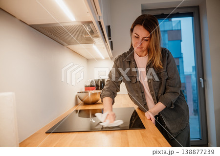 Woman cleans kitchen counter in a modern apartment during evening hours Woman cleans kitchen counter in a modern apartment during evening hours 138877239