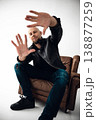 Man sits on chair and poses with hands extended in a studio setting 138877259