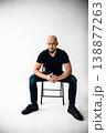 Man sits on chair in studio with plain background during a photo session in daylight 138877263