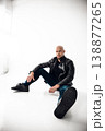 Man sits on floor wearing black leather jacket and jeans in a bright room with white walls 138877265